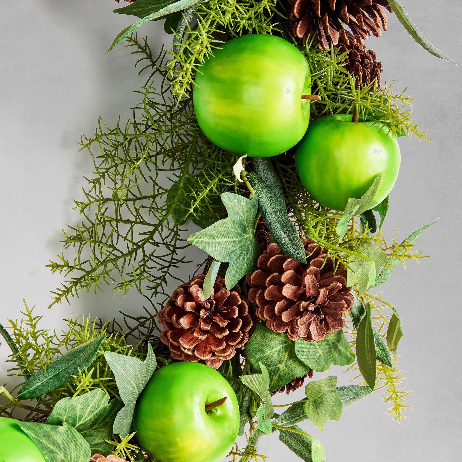 24" faux green apple and mixed botanicals wreath, closeup view, with gray background.