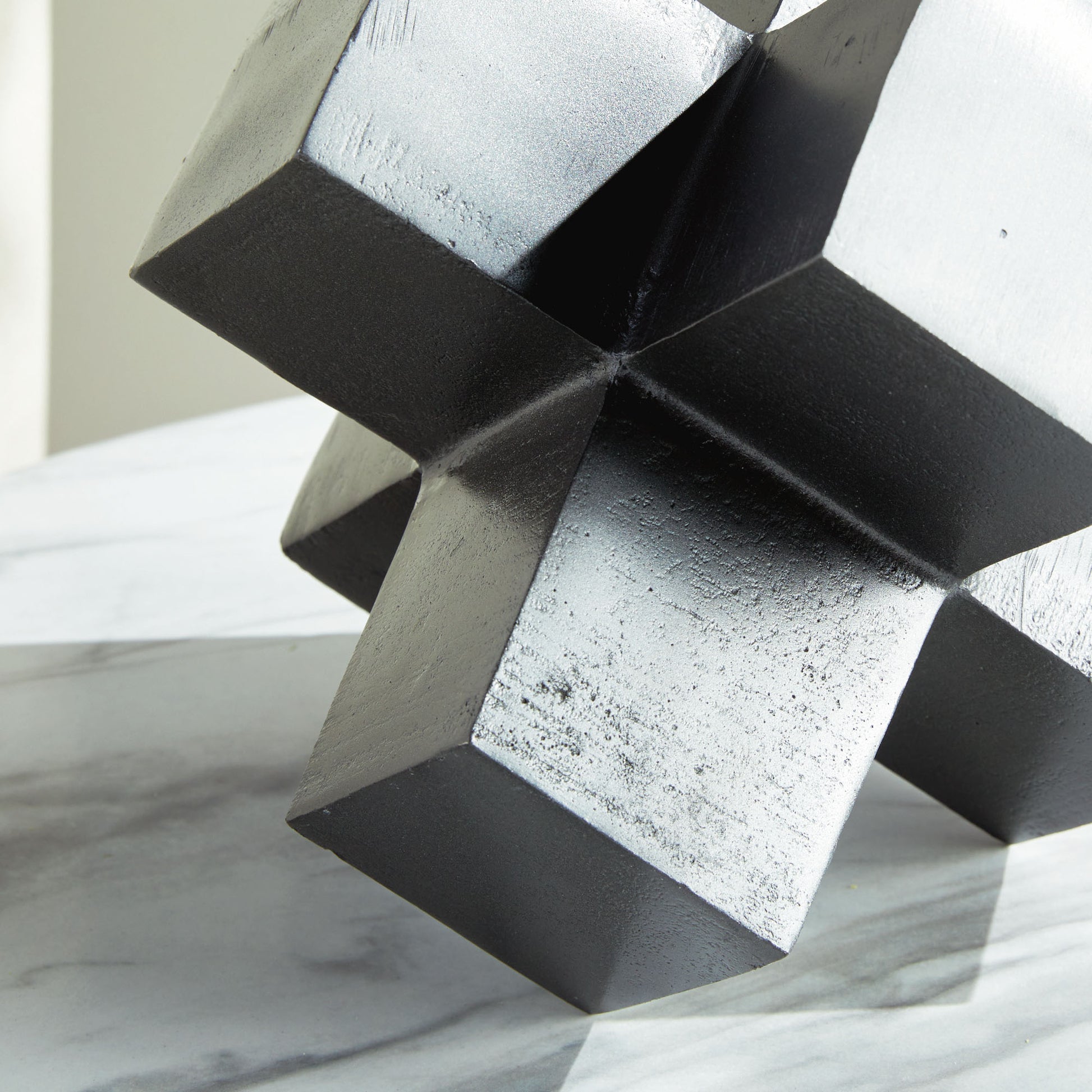 Closeup view of silver geometric plus sign decorative object on marble table.