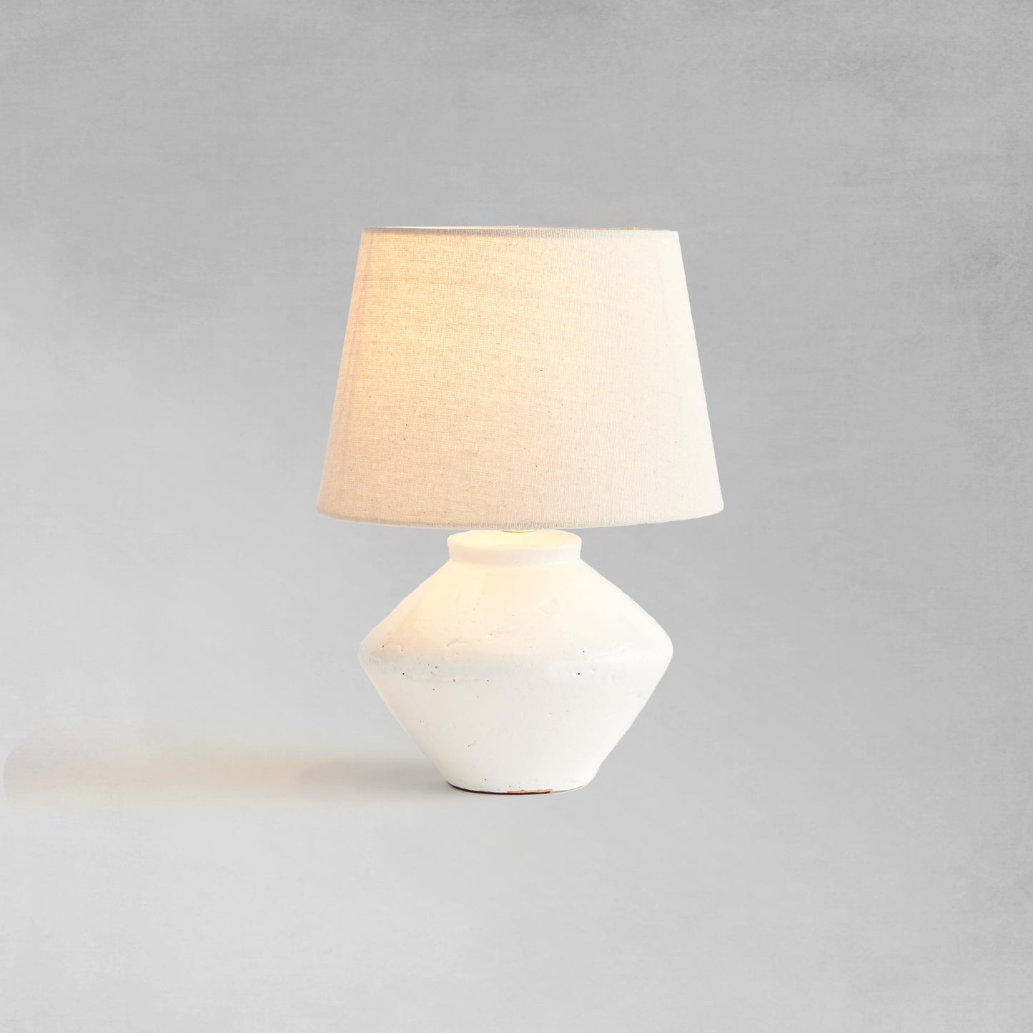 Glazed white mini lamp, illuminated, with gray background.