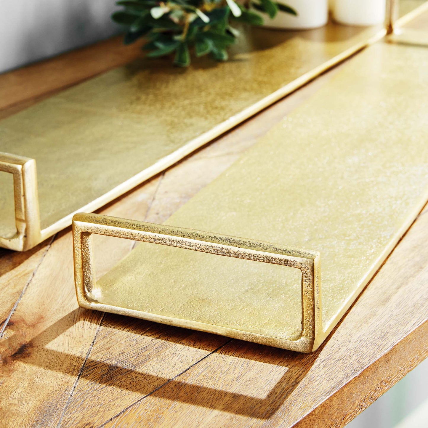 Gold narrow metal trays, set of two, closeup view, stylized on table.