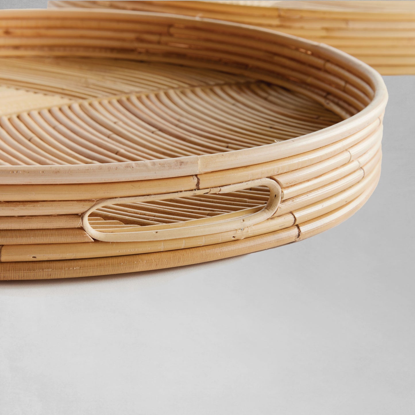 Handwoven round rattan serving trays, closeup view, with gray background.