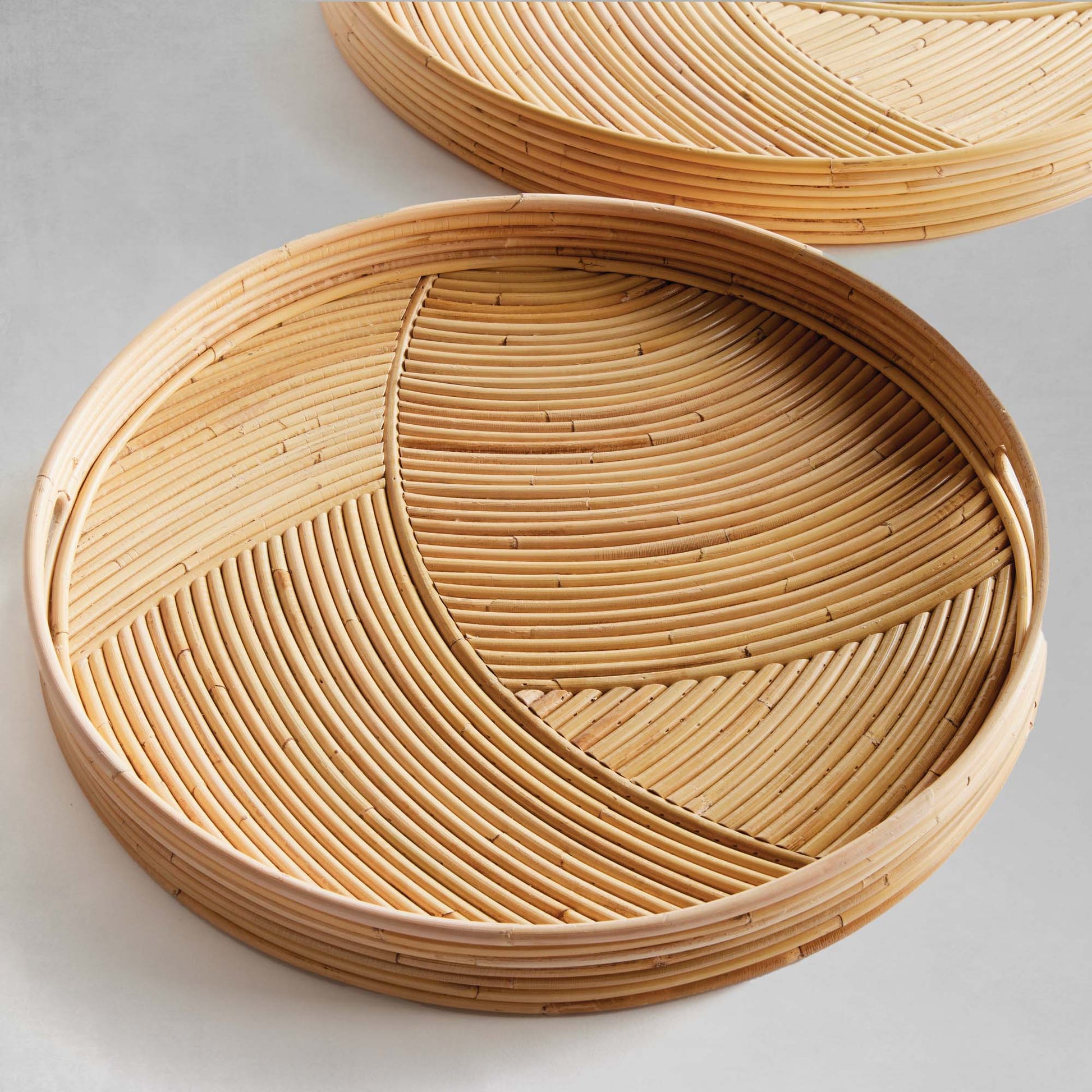 Handwoven round rattan serving trays, top view, with gray background.