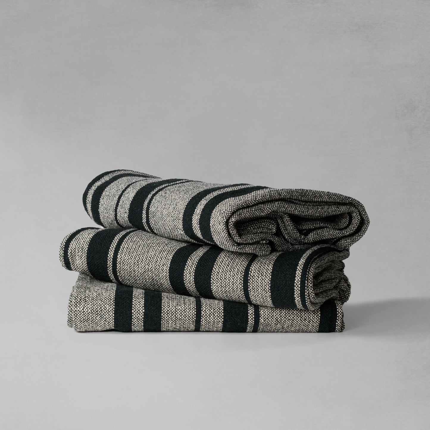 Handwoven striped cotton throw blanket, stacked together, with gray background.