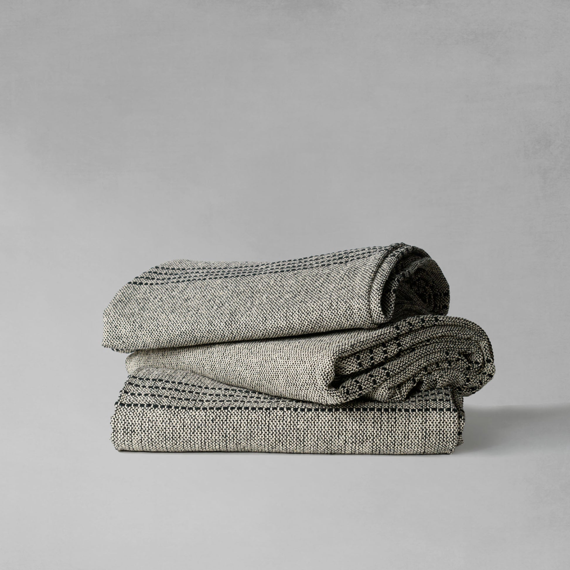 Handwoven ticked stripe cotton throw blanket, stacked together, with gray background.