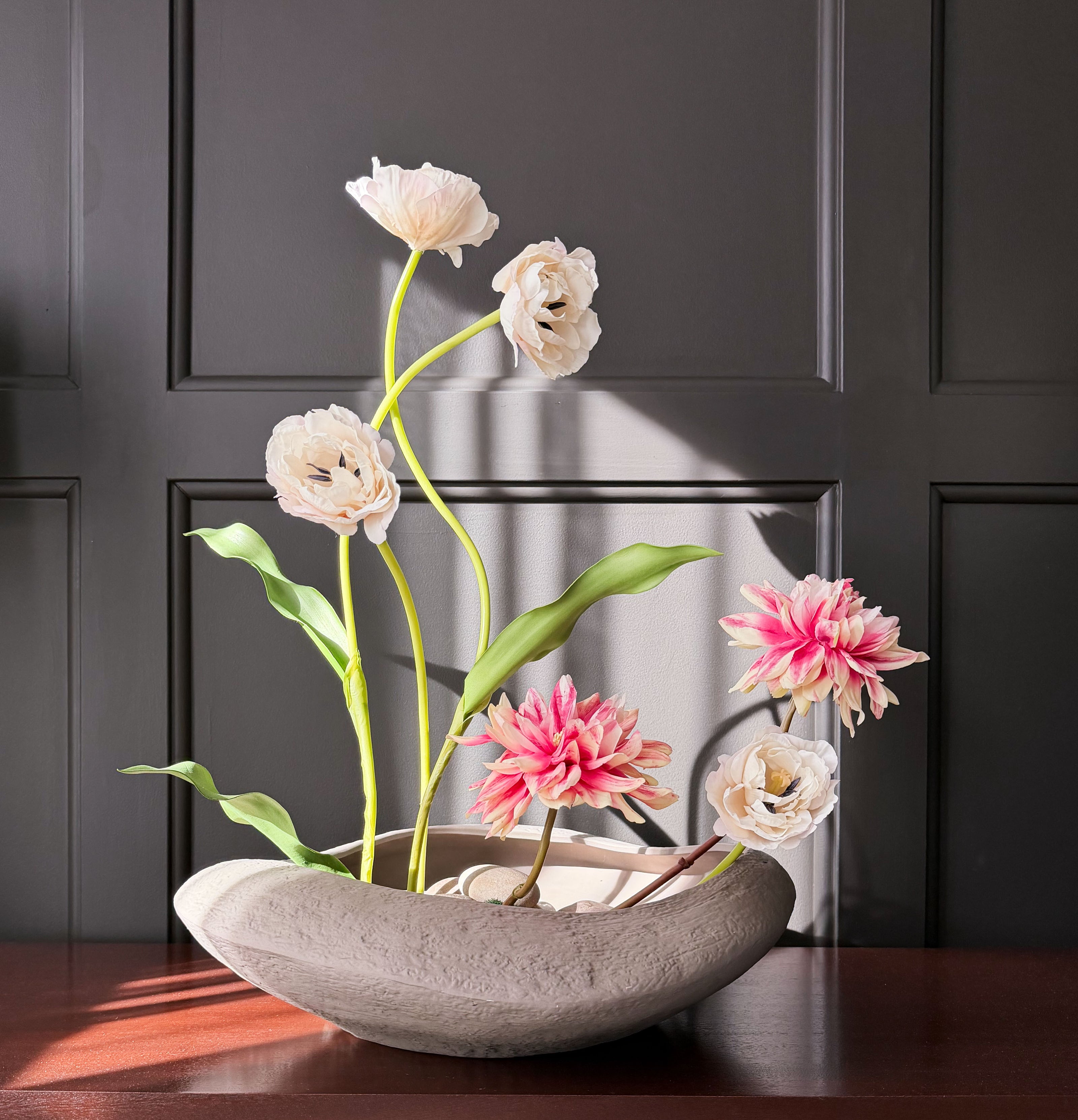 Decorative flower arrangement in a stone bowl on a wooden surface with a dark panel background