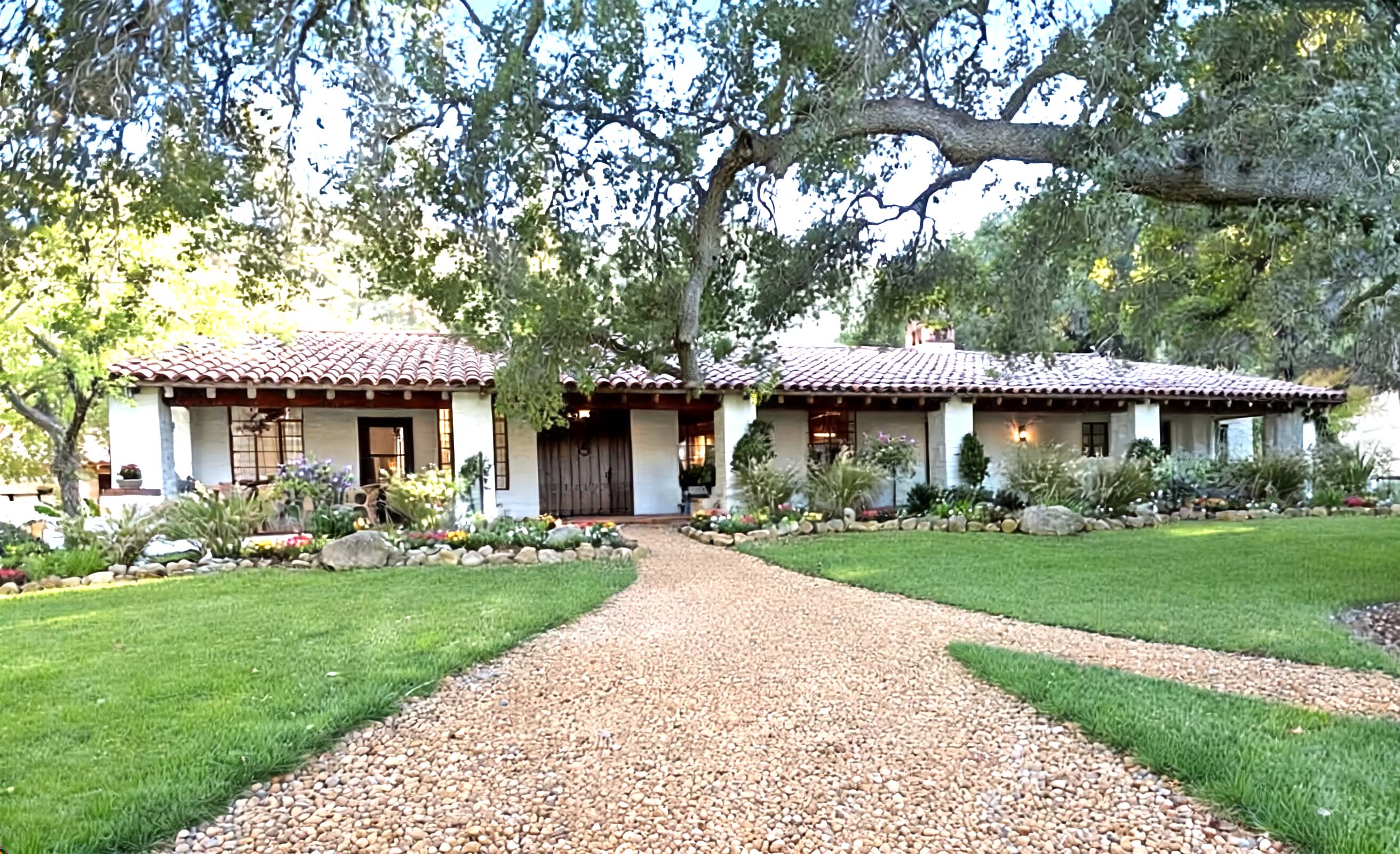 Stately home with a gravel driveway leading to a front door, surrounded by greenery.
