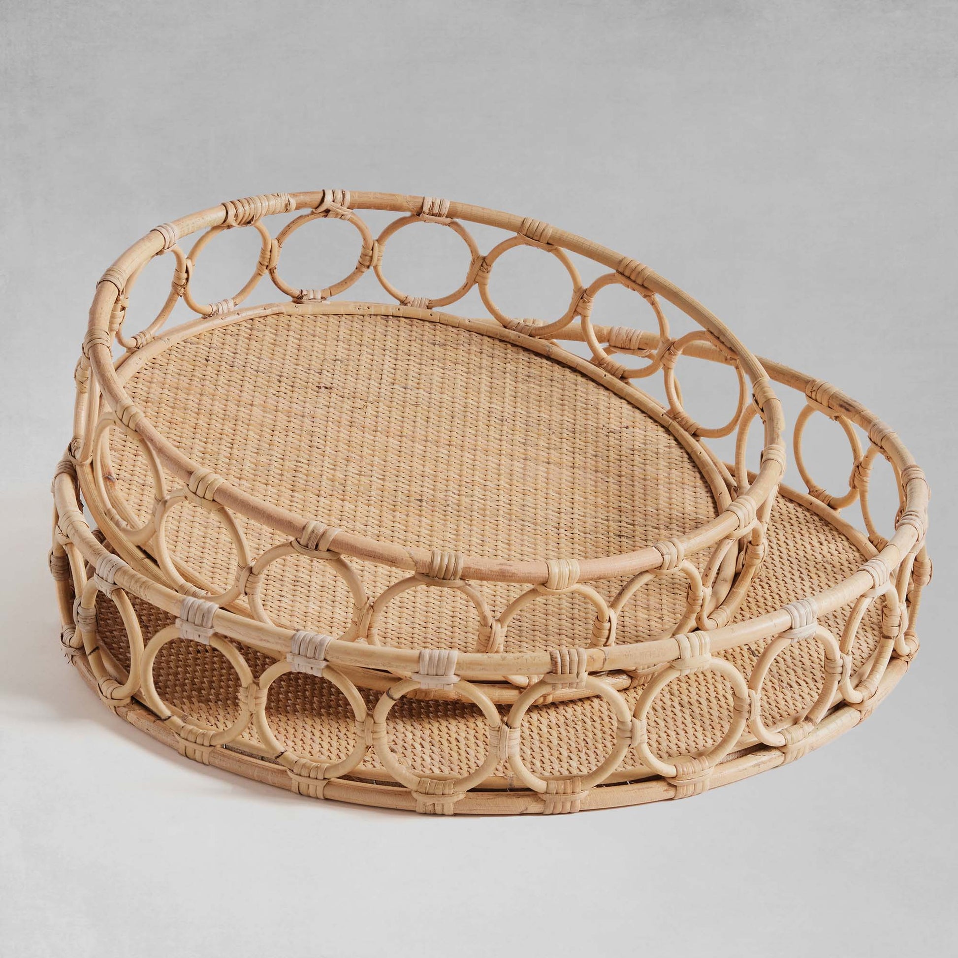Lattice round rattan serving trays stacked with gray background.