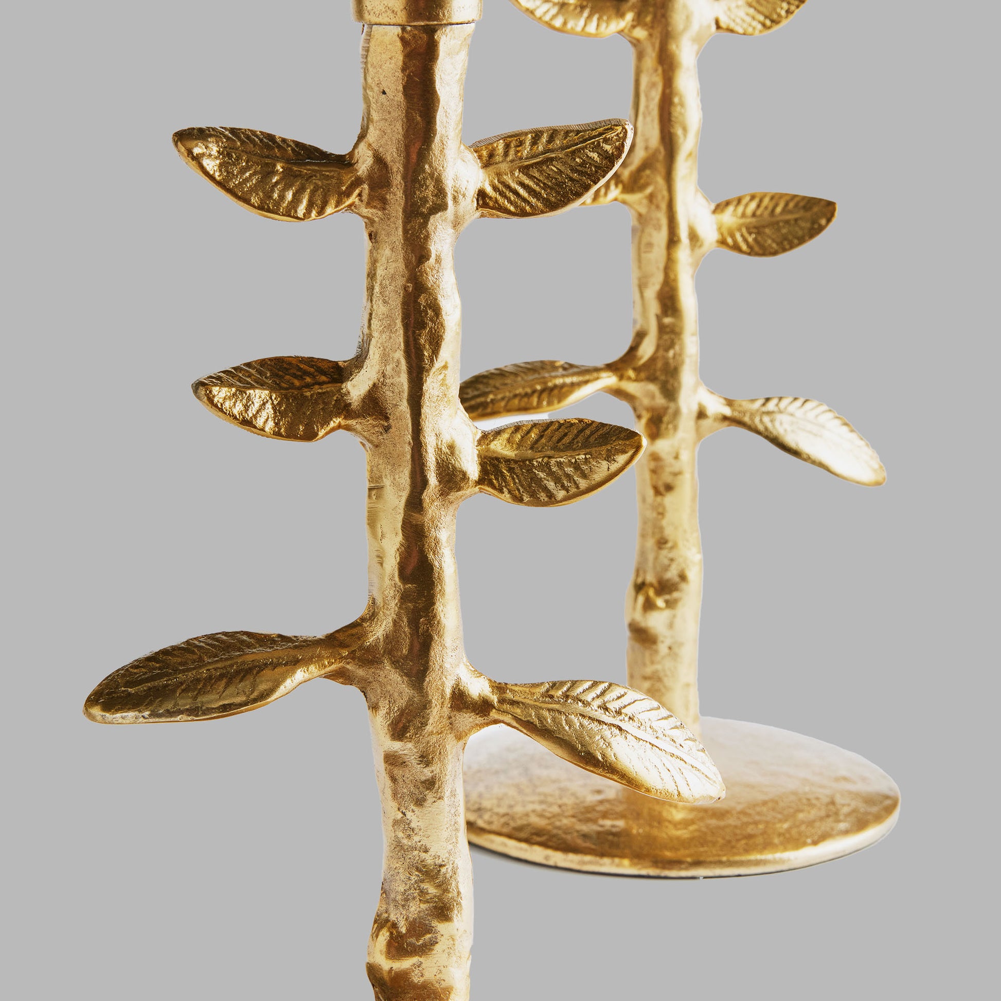 Closeup view of leaves and trunk of a set of two leaf candleholders in gold.