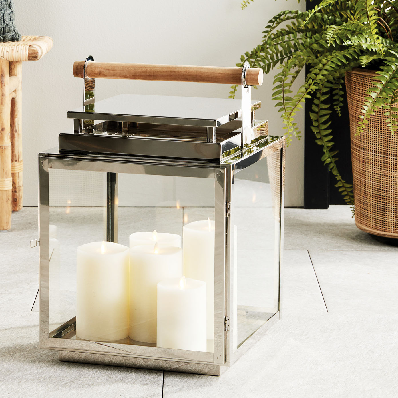 Large metal outdoor lantern with chrome finish on floor with plant in background.