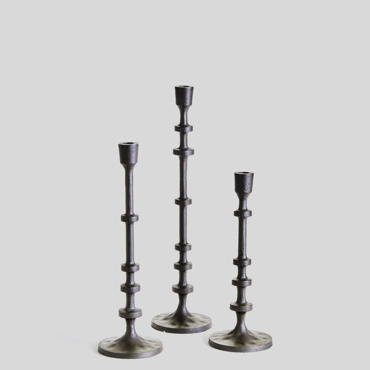 Set of three minimalist taper candleholders in bronze finish with gray background.