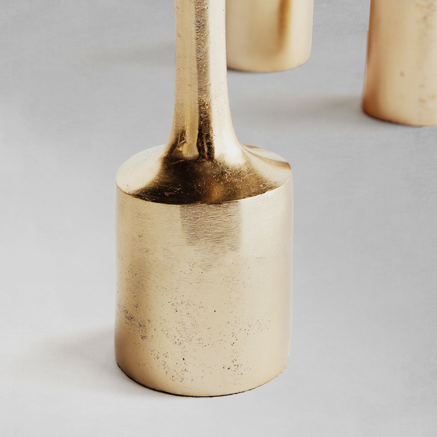 Modern gold taper candleholders, set of 3, closeup view of candle base, with gray background.