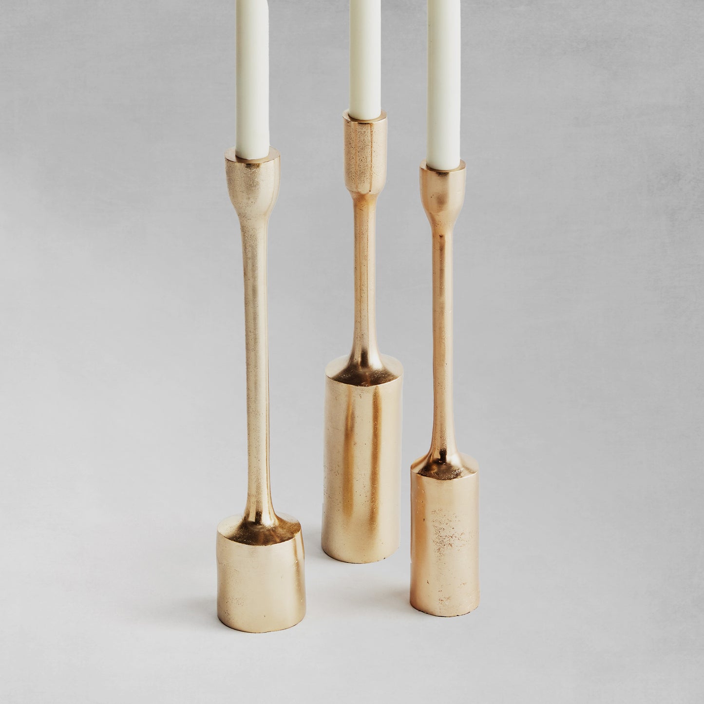 Modern gold taper candleholders, set of 3, with gray background.