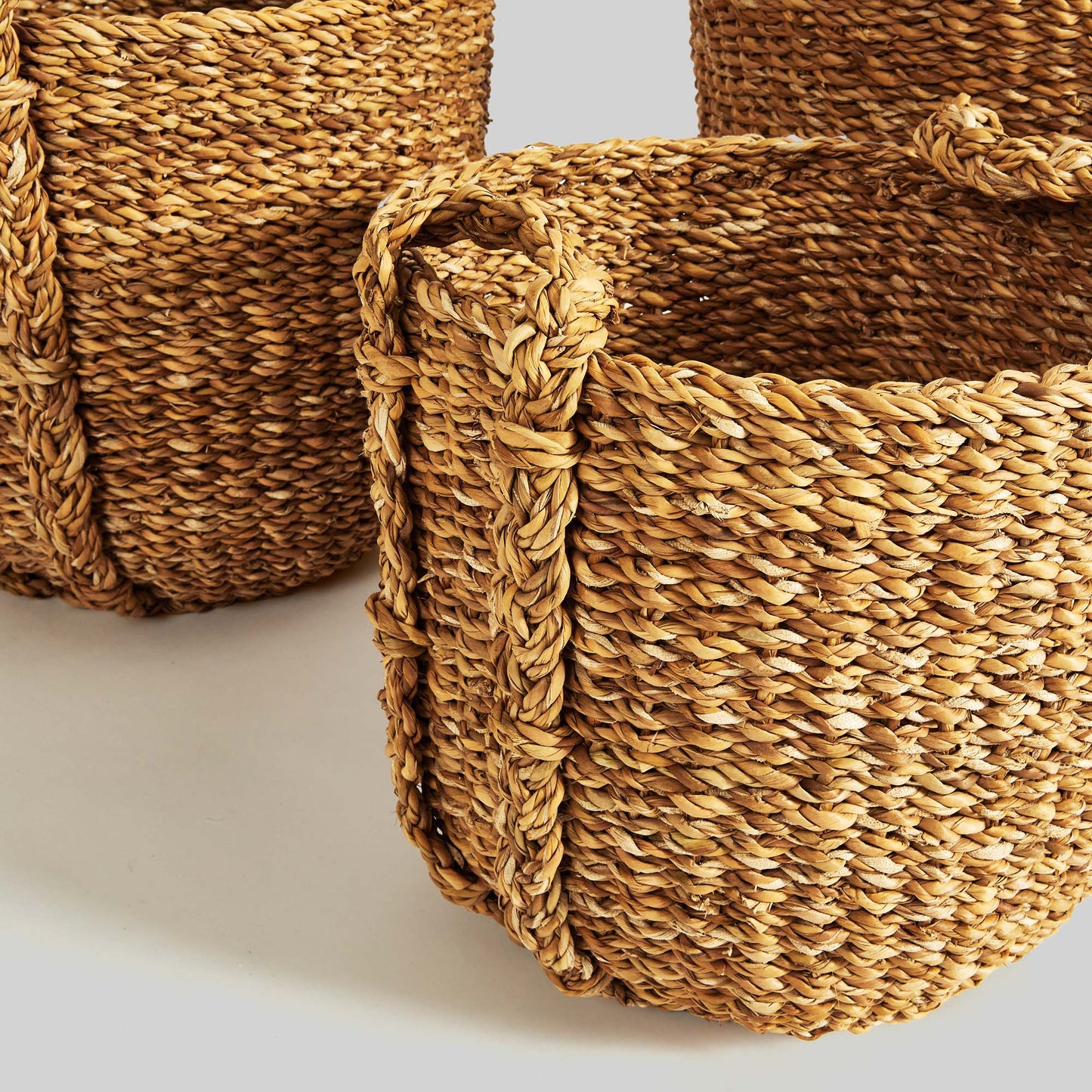 Natural woven seagrass drum baskets, closeup side view, with gray background.