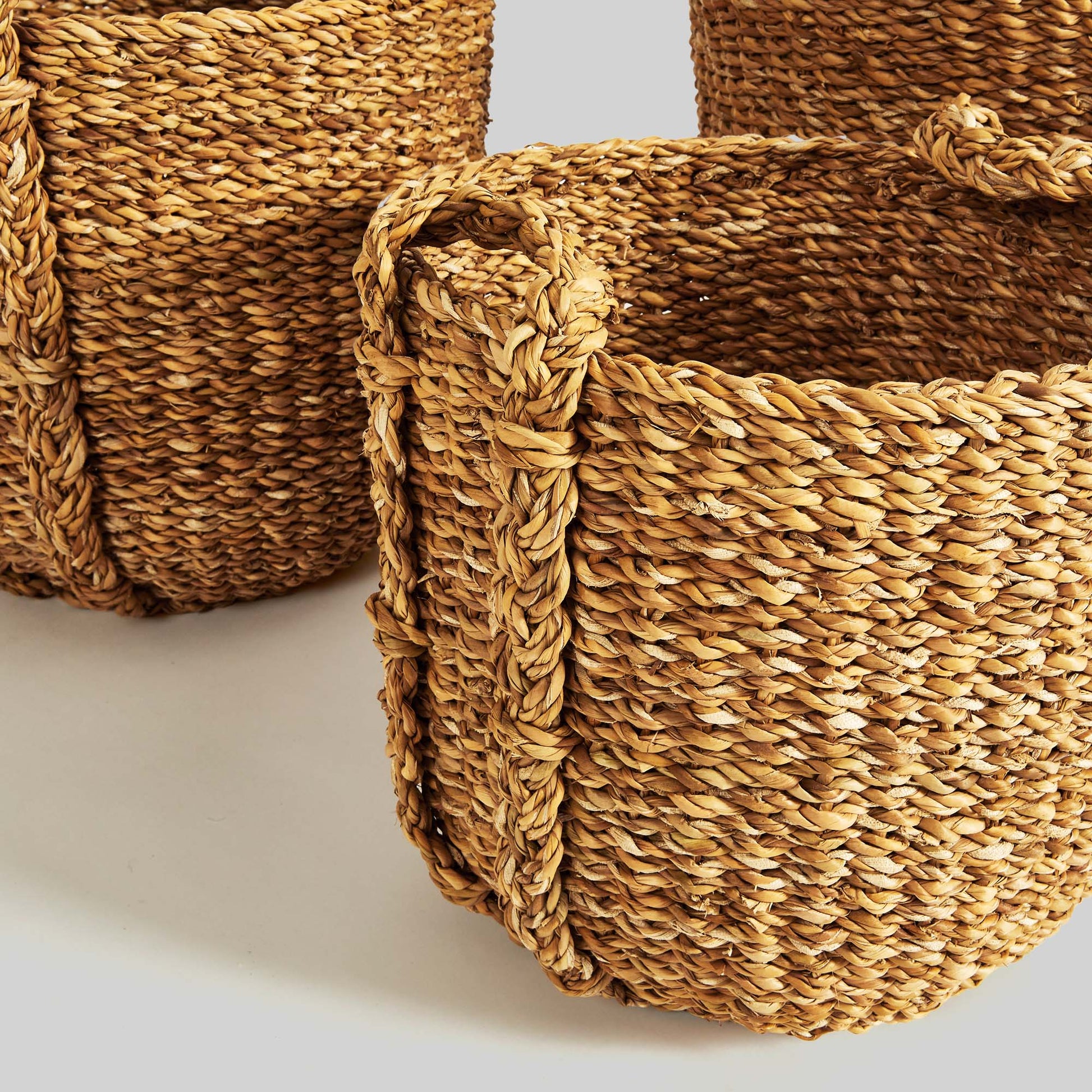 Natural woven seagrass drum baskets, closeup side view, with gray background.