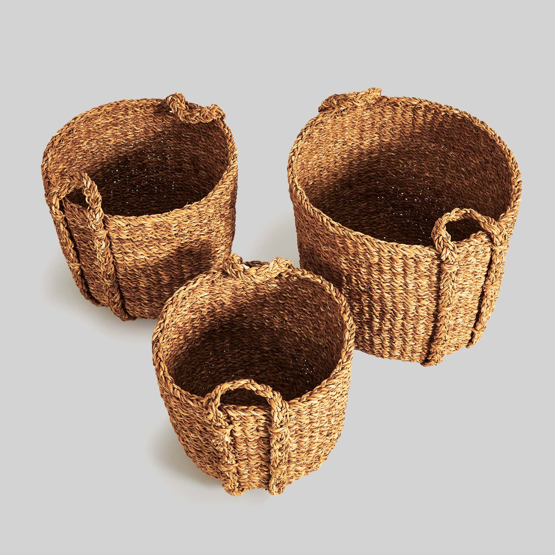 Natural woven seagrass drum baskets, top view, with gray background.