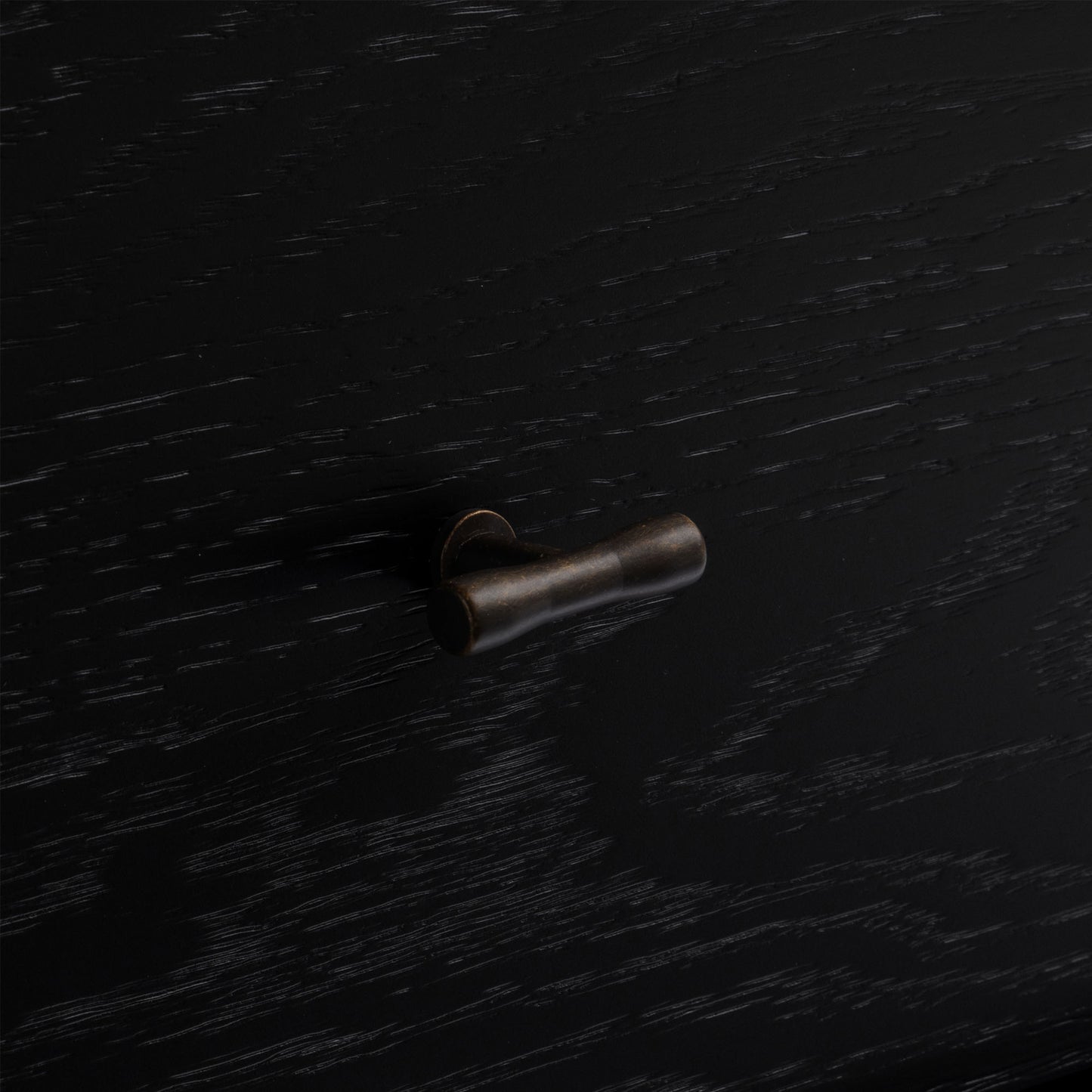 Bronze cabinet knob on a black wood nightstand.