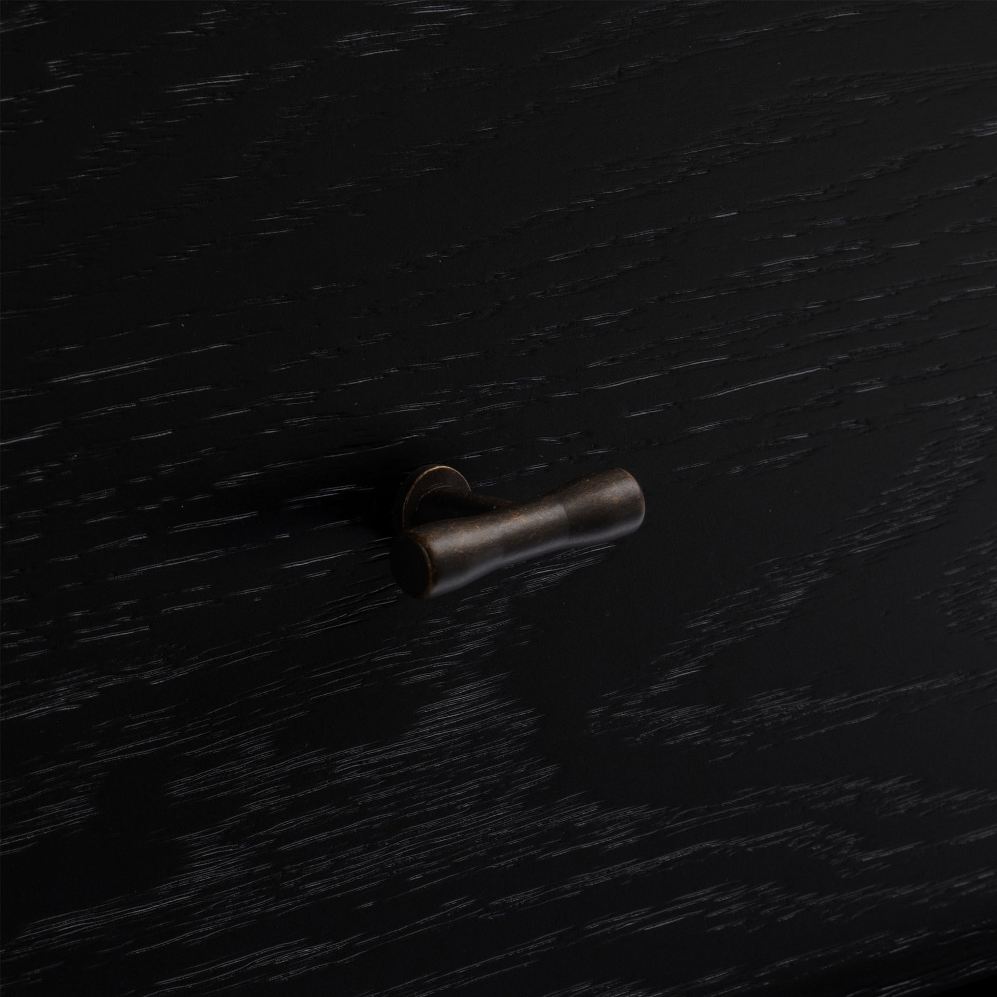 Bronze cabinet knob on a black wood nightstand.