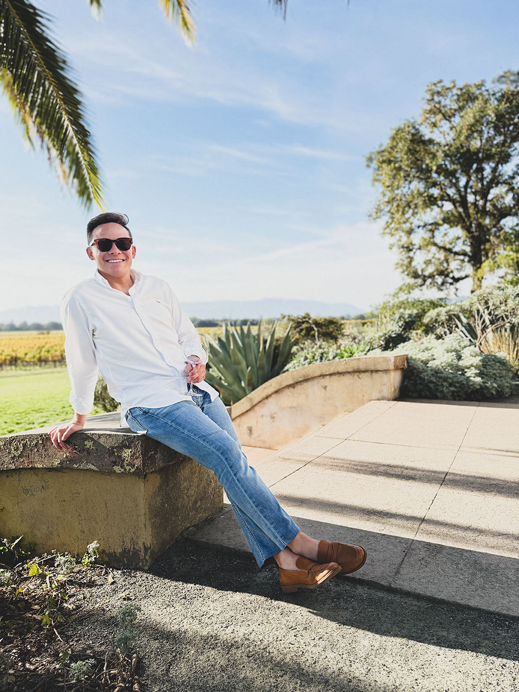 Adam Gibbs, co-founder at parker + gibbs, holding a wine glass sitting on a wall outside at Scribe Winery in Sonoma, California.