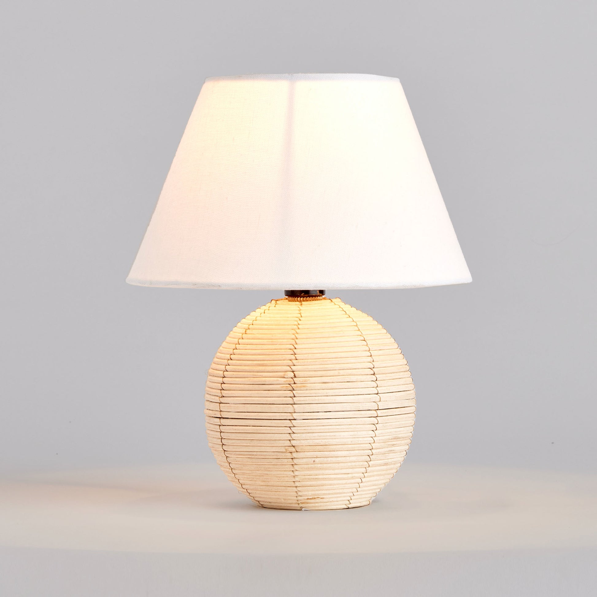 Rattan mini lamp, illuminated, with gray background.