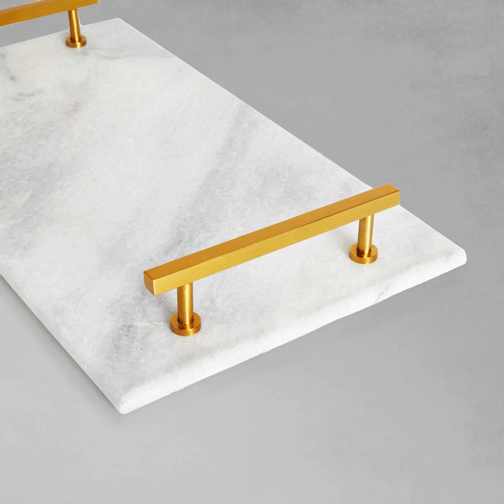 Rectangular marble serving tray with brass accents, closeup view of handle, with gray background.