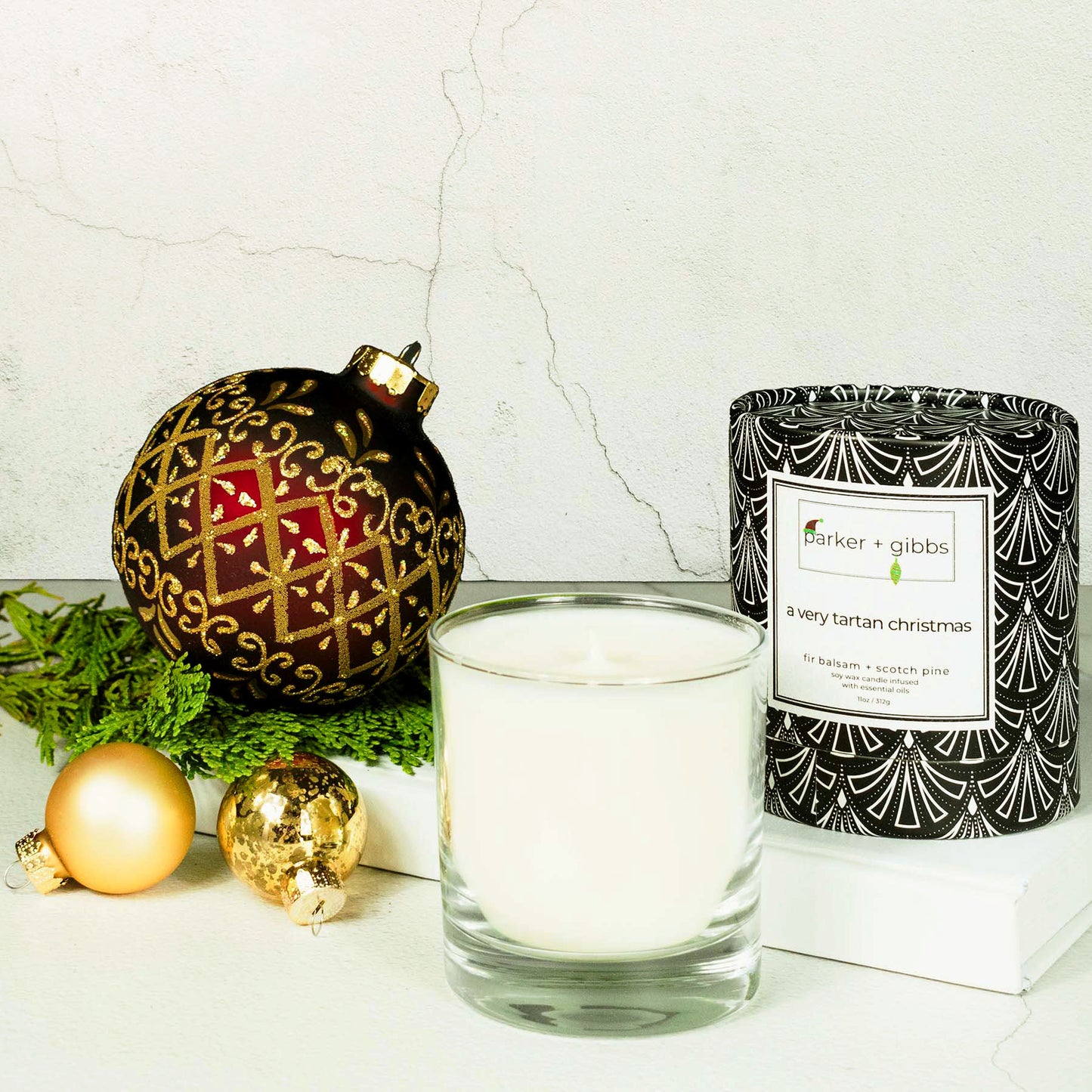 Scented soy holiday candle on limestone table with white book, garland, and christmas ornaments.