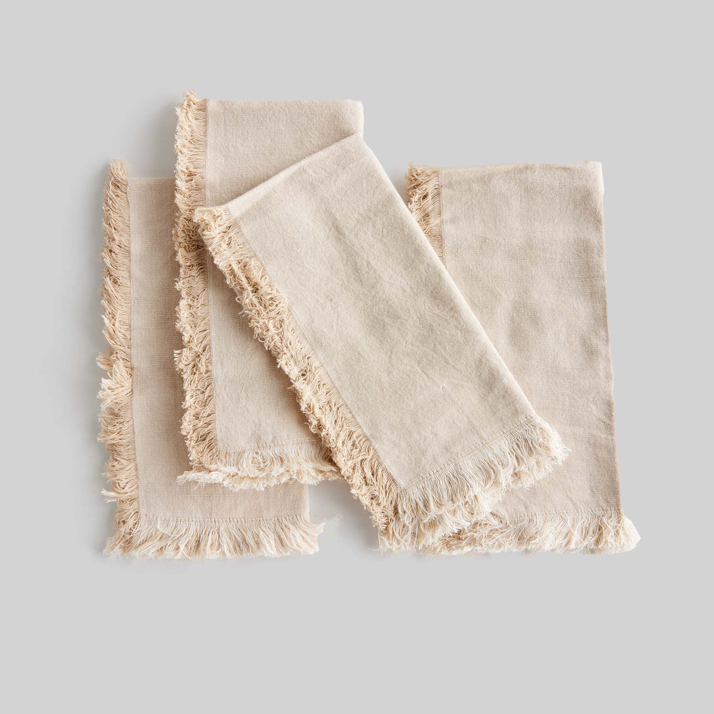 Tan fringe square cotton dinner napkins set of 4, laying flat, with gray background.