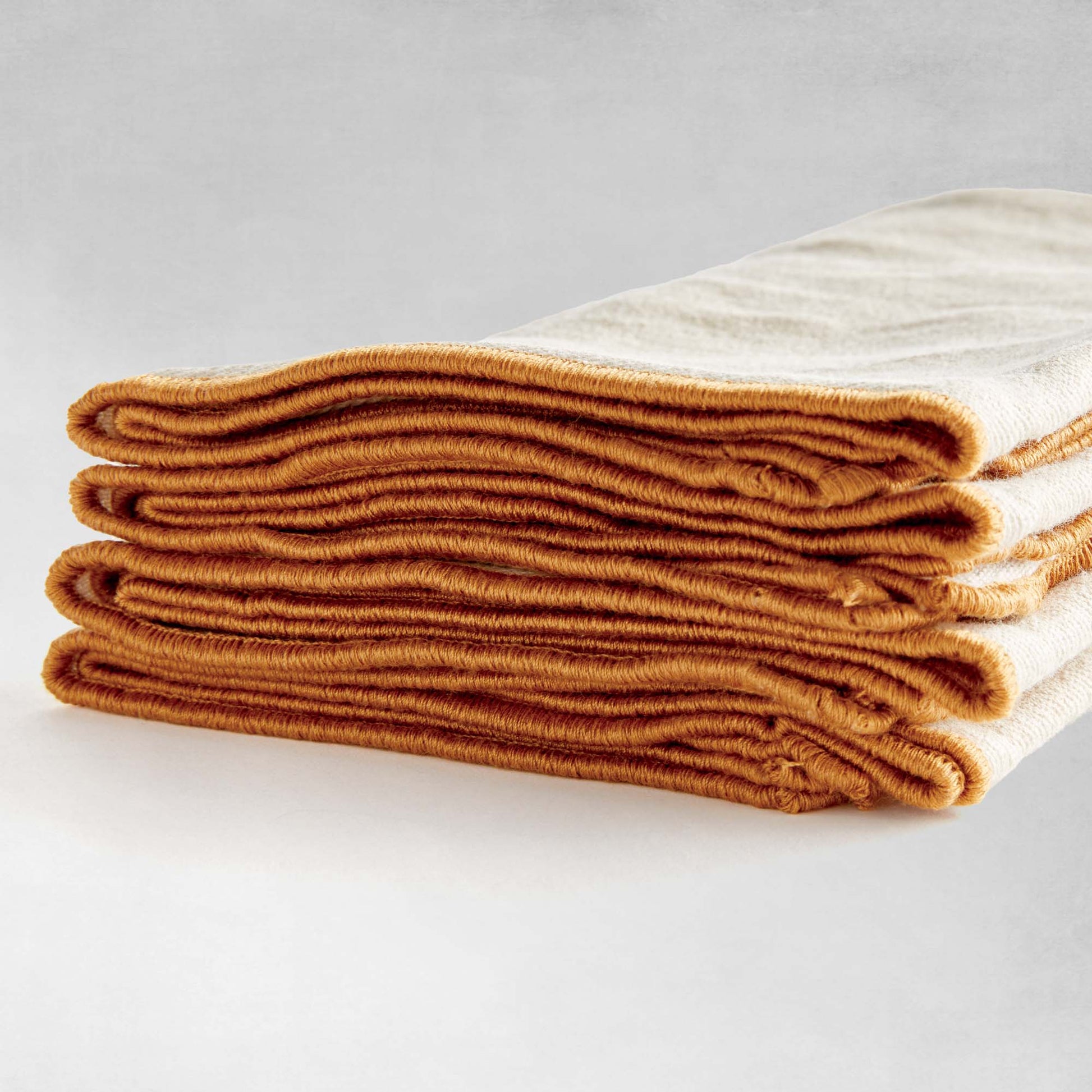 Tan square cotton dinner napkins, set of 4, edge finishing closeup view, with gray background.