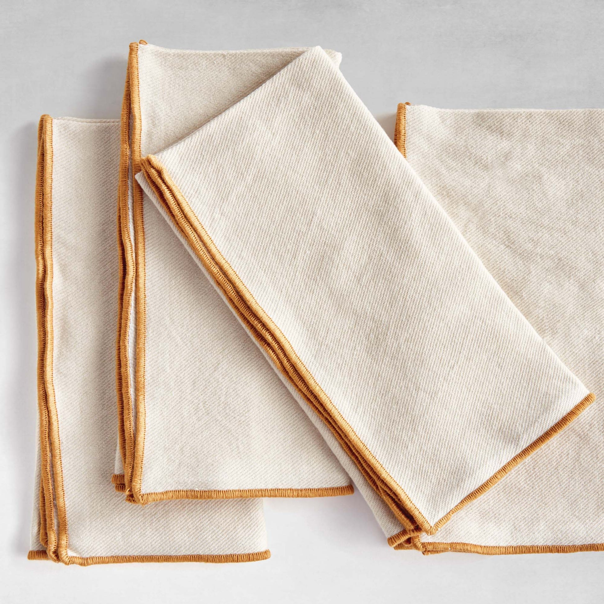 Tan square cotton dinner napkins, set of 4, top view, with gray background.