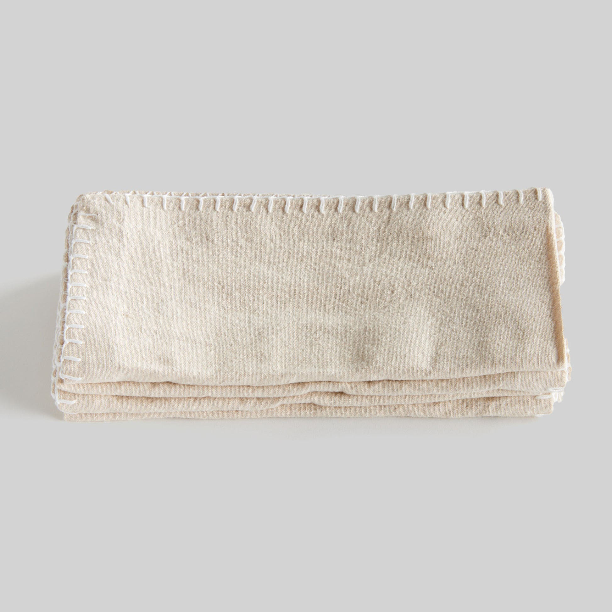 Taupe whipstitch square cotton dinner napkins set of 4, folded and stacked on top of each other, with gray background.