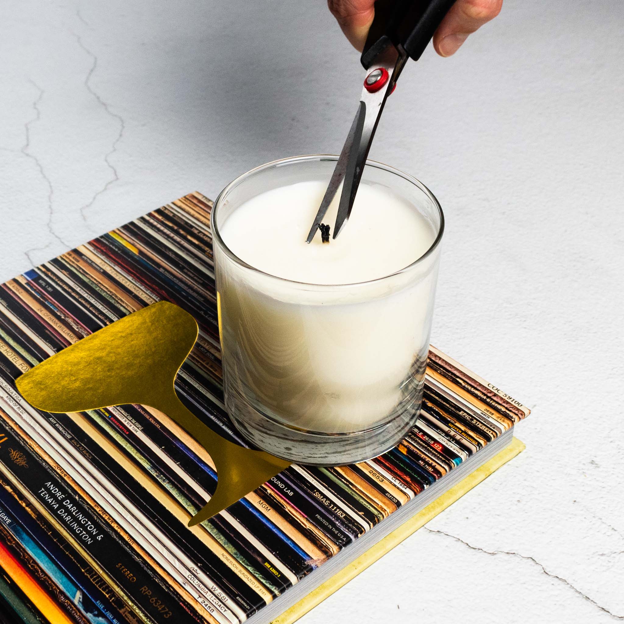 Trimming candle wick on top of Booze and Vinyl book on limestone table.