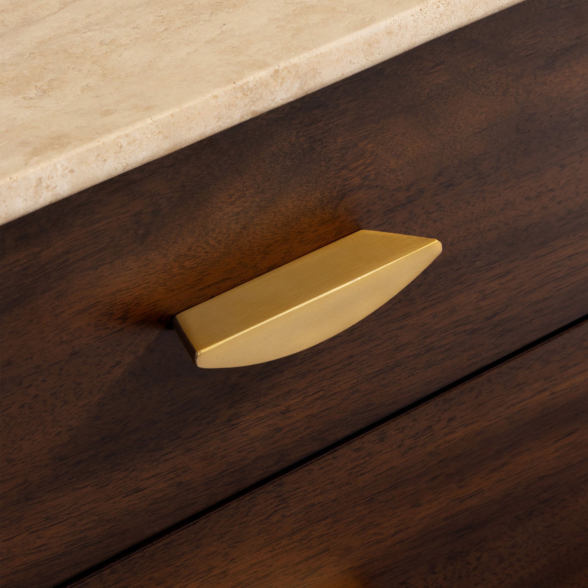 Gold cabinet handle on a wooden drawer with a travertine top.