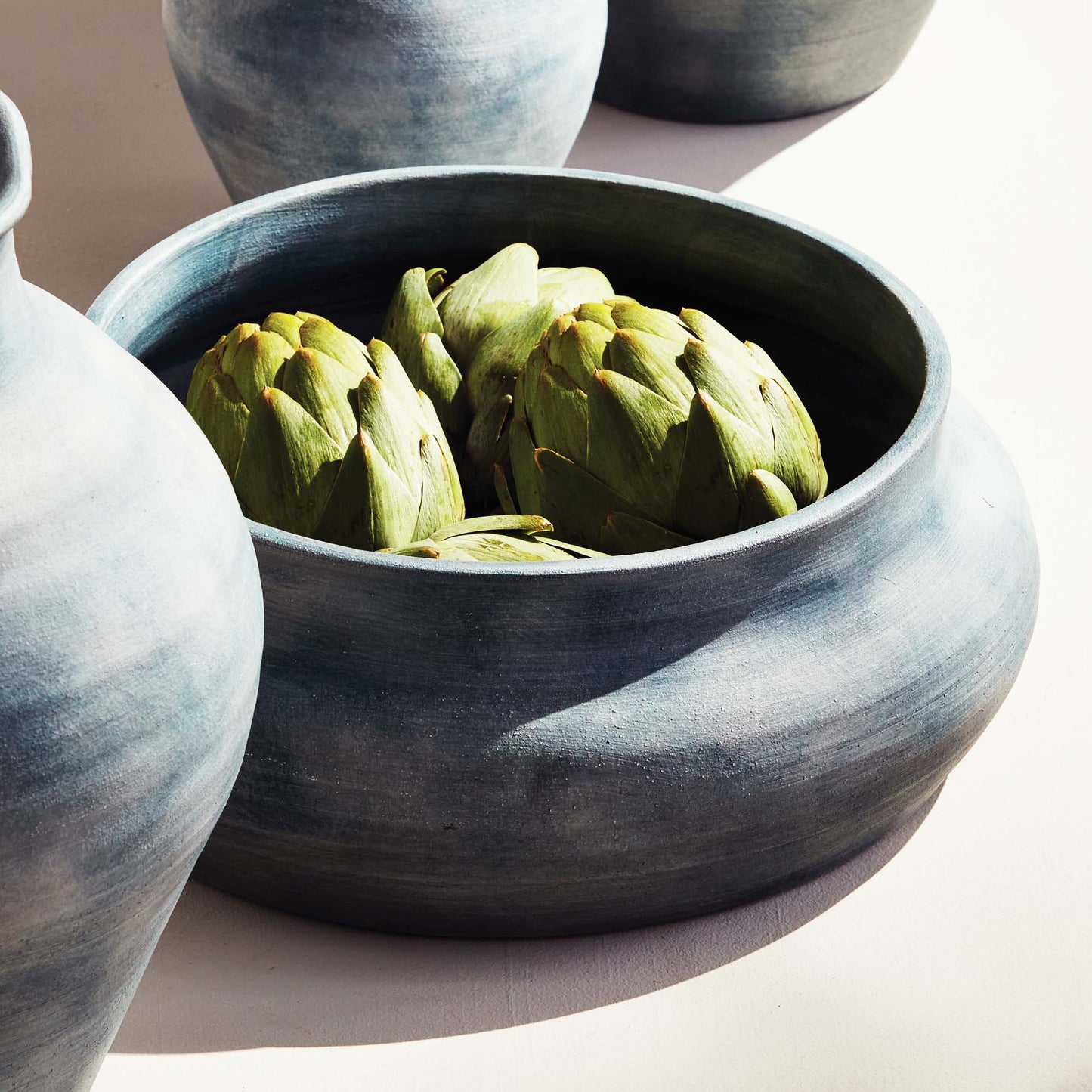 Weathered blue-gray terracotta decorative bowl stylized with artichokes on table.