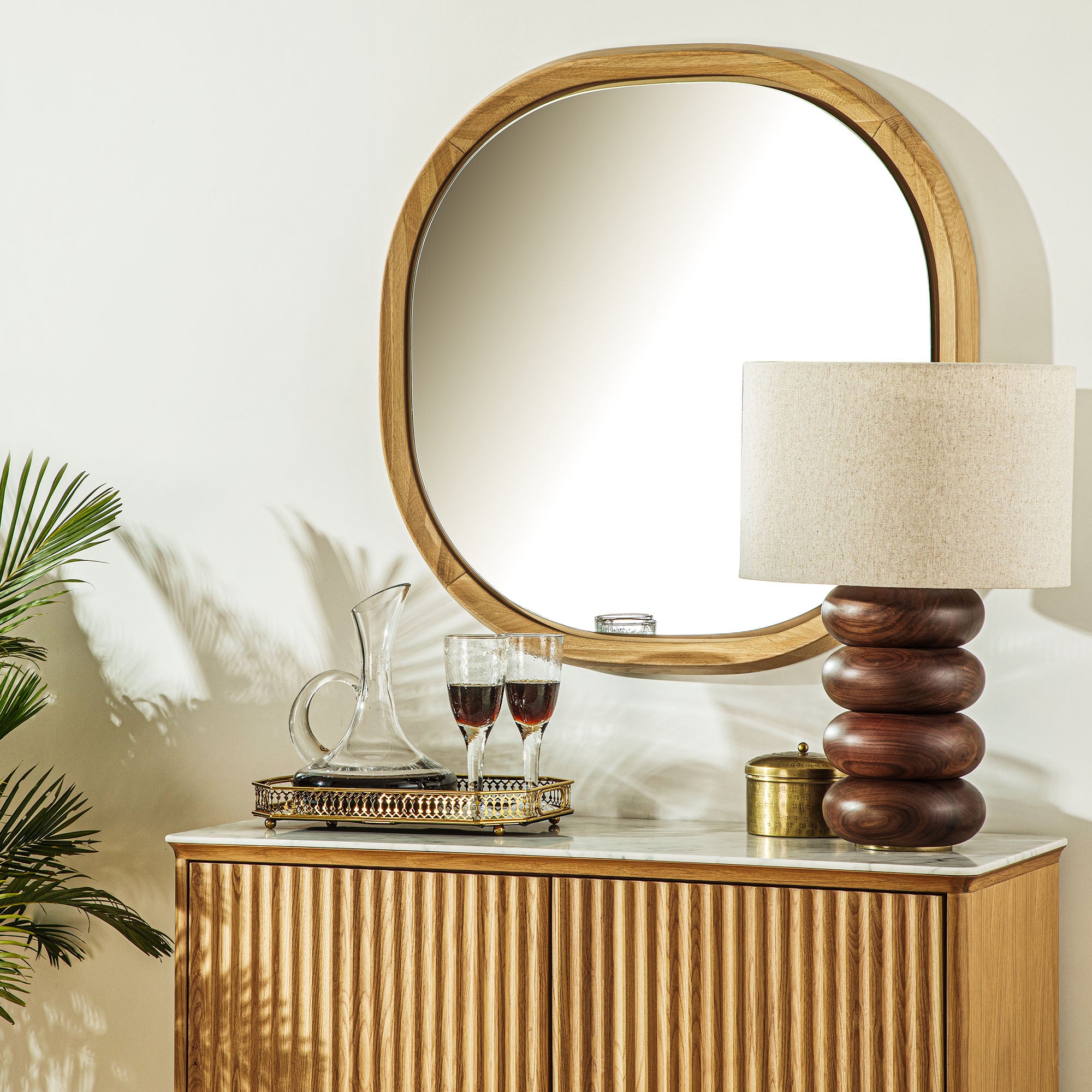 Vignette with fluted console table, decorative tray with a decanter and wine glasses, a table lamp, and a light oak wooden mirror.