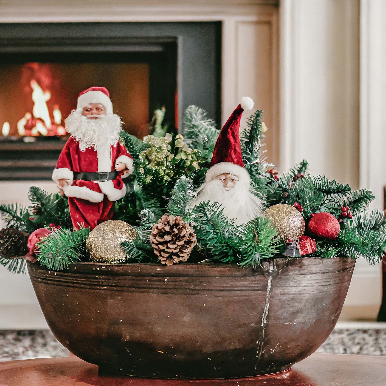 Wooden dough bowl filled with christmas ornaments, Santa Claus, greenery, and ornaments.