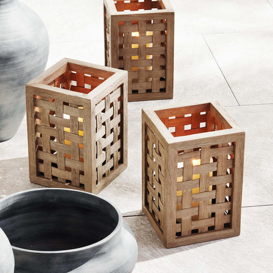 Woven teak hurricane candleholders stylized on patio with large gray ceramic planters.