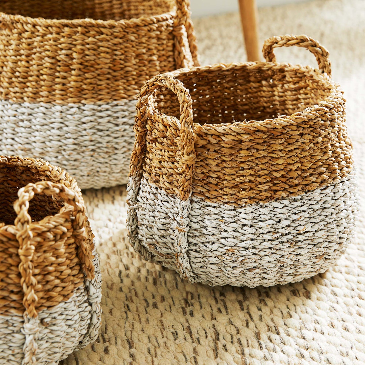 Woven two-tone seagrass baskets, closeup view, stylized on rug.