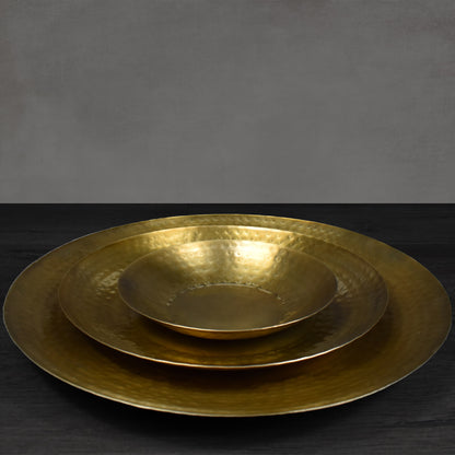 Set of three nested, round antiqued brass metal hammered tray on dark wooden floor.