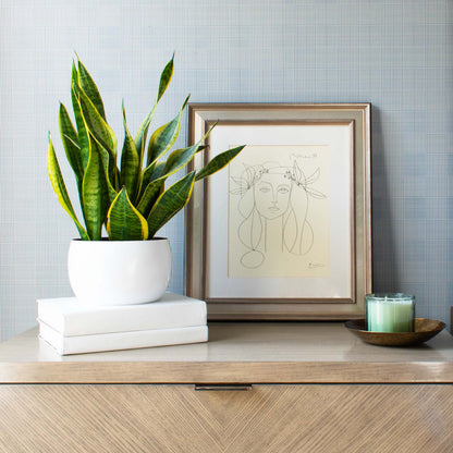 White enamel painted vessel with antique brass finish interior on top of white painted books, candle on top of hammered antique brass finish tray, with leaning Picasso drawing in background.