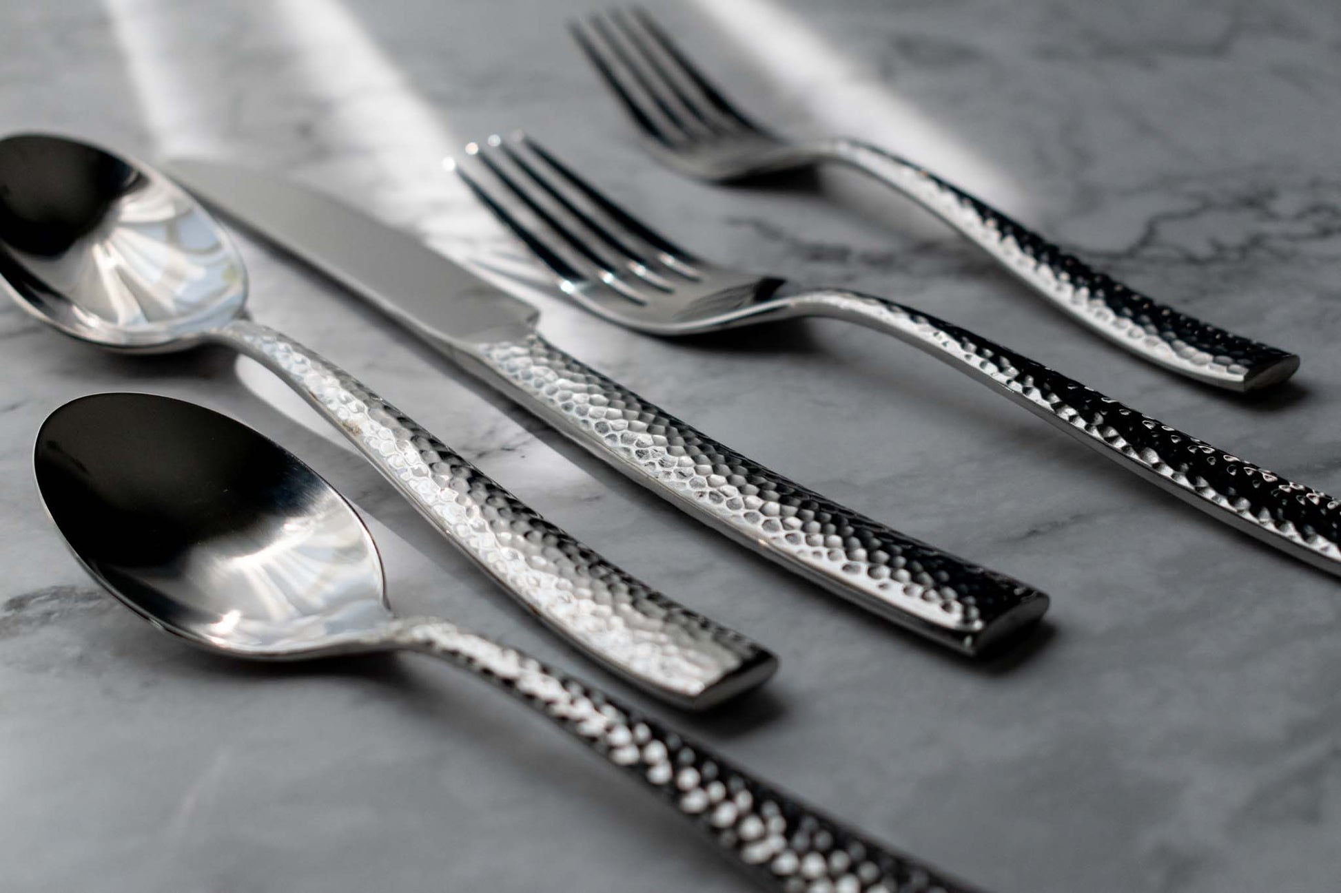 https://parkergibbs.com/cdn/shop/products/burton-shiny-polished-silver-hammered-contemporary-flatware-cutlery-set-on-marble-table.jpg?v=1653016057&width=1946