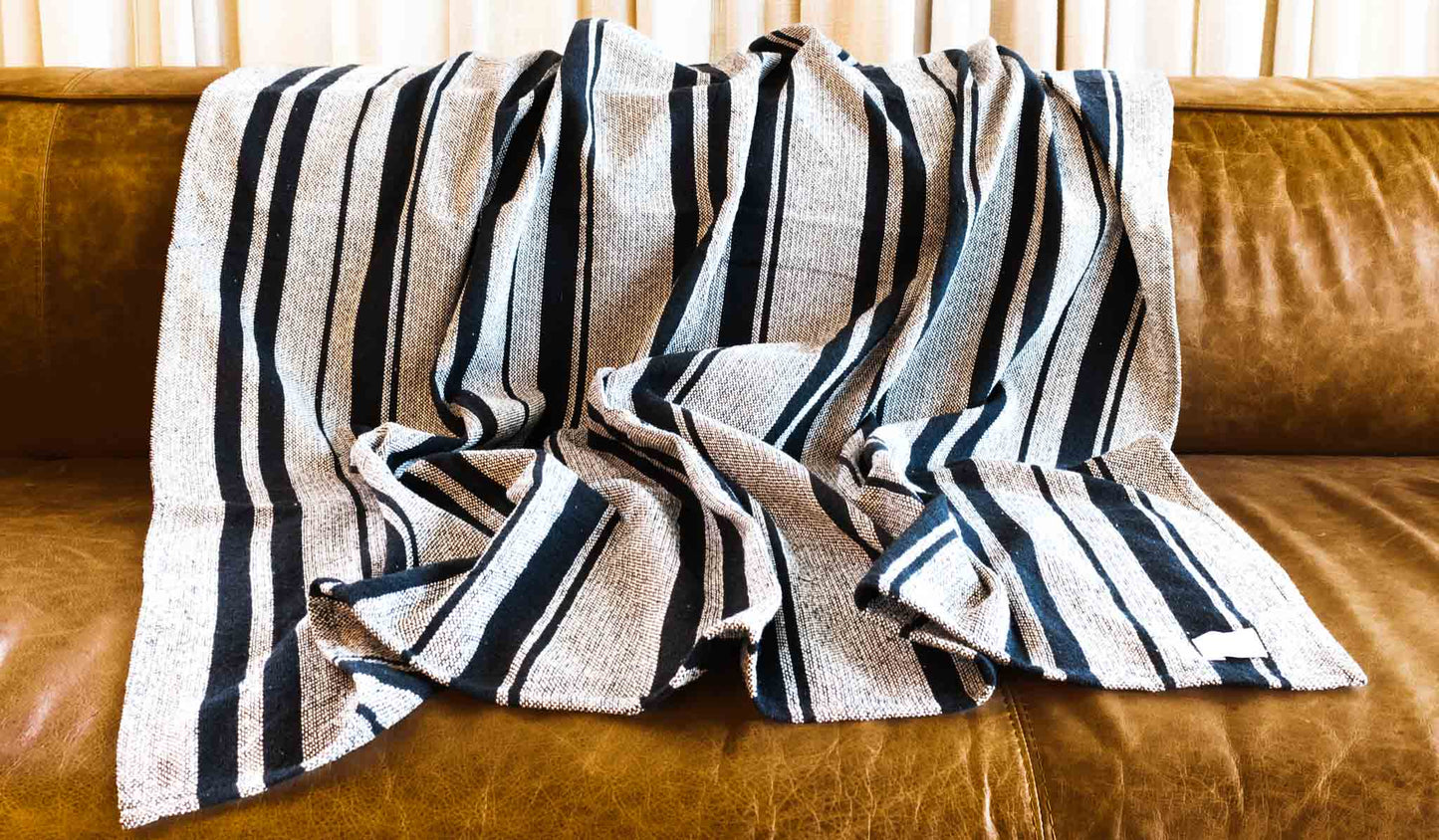 Cotton throw blanket with sand and black stripes on leather sofa.