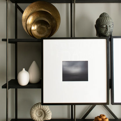 Set of three nested, round antiqued brass metal hammered trays on black oak bookshelf with decorative objects.