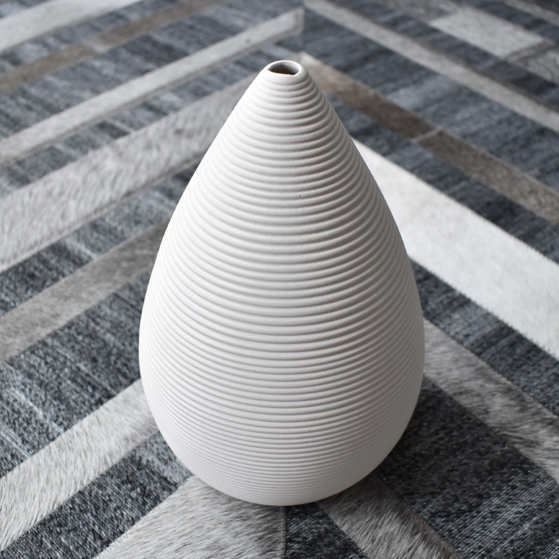 Tapered ribbed matte white ceramic vase on chevron cowhide rug.